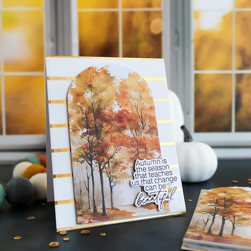Autumn-themed card with trees and pumpkin on a table with blurred autumn background